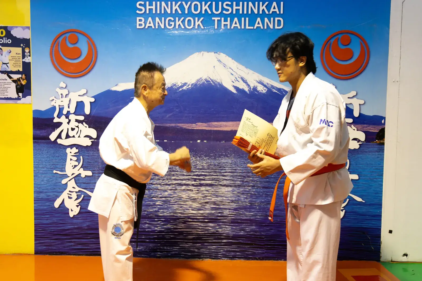 Shihan Nagashima โค้งคำนับขณะมอบสายสีส้มและใบประกาศให้นักเรียน หน้าฉาก Shinkyokushinkai Bangkok Thailand