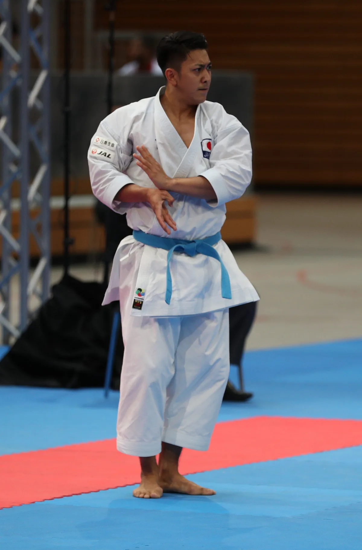 A male karateka standing barefoot on the mat in the middle of a kata, arms crossed