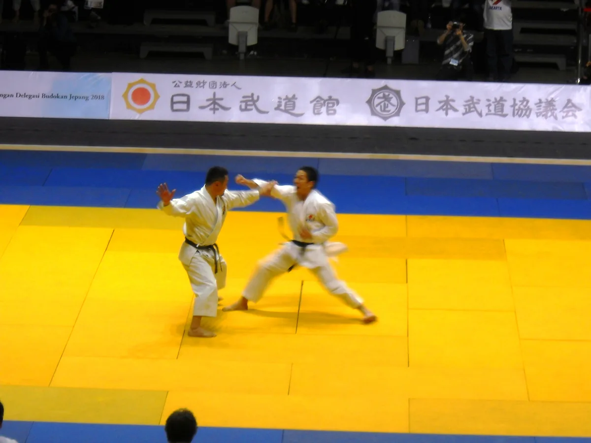 两名空手道练习者在黄色垫上演示不接触的技术,上方是日本武道馆和日本武道协议会的横幅