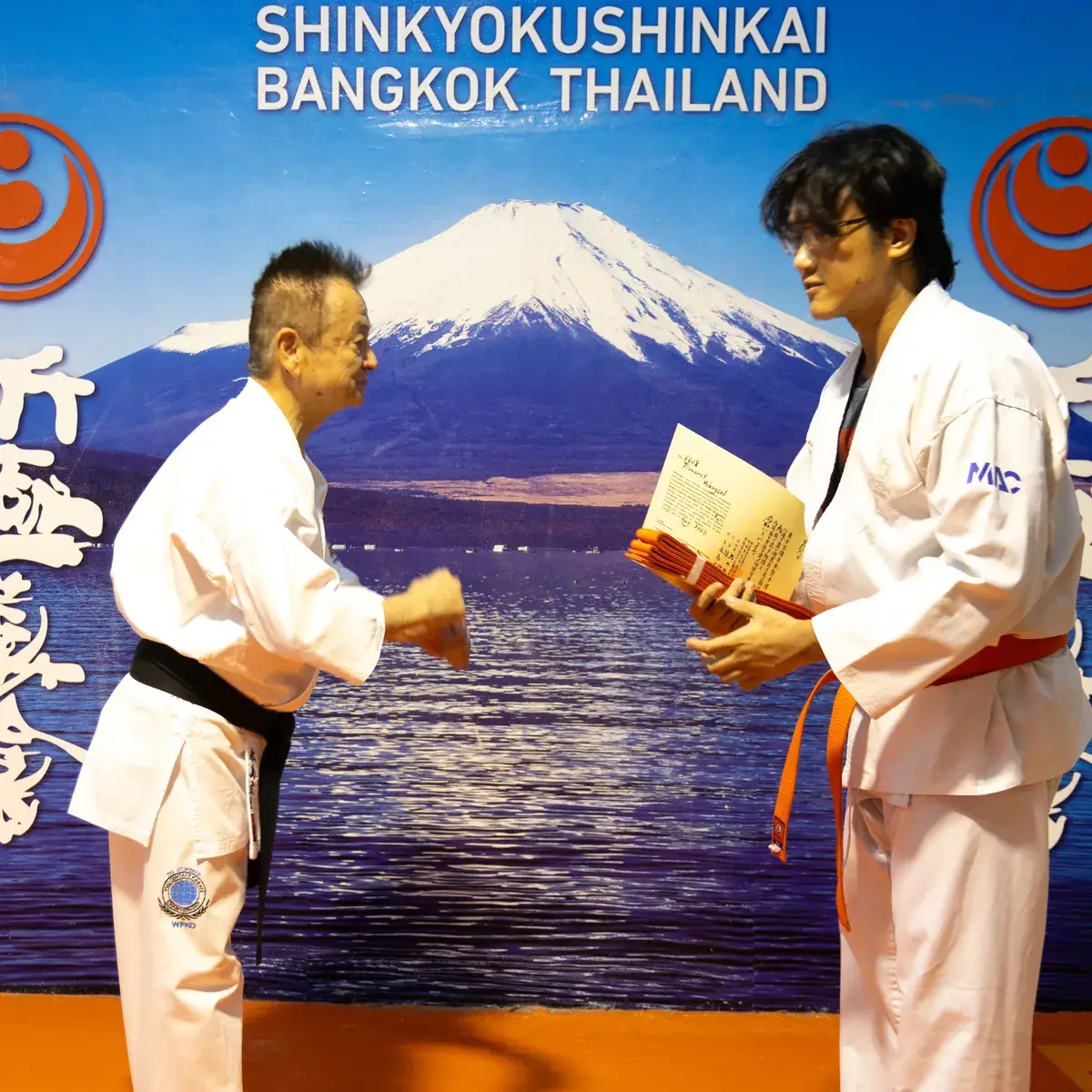 Shihan Nagashima โค้งคำนับขณะมอบสายสีส้มและใบประกาศผลสอบรอบ 21 สิงหาคม ให้นักเรียนหน้าฉาก Shinkyokushinkai Bangkok Thailand