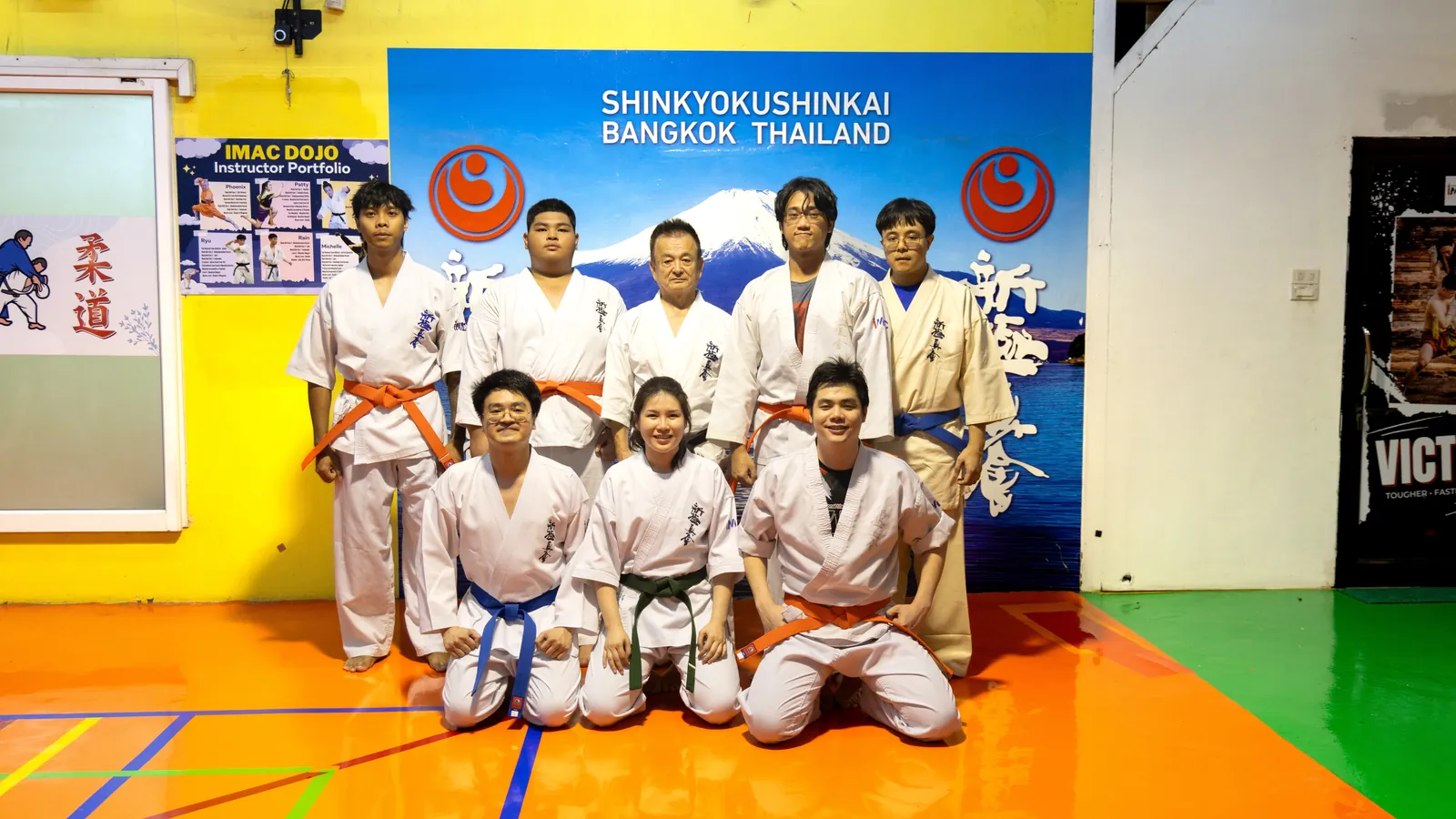 Those who passed the 21 August grading photographed with Shihan Nagashima Fumiaki in front of the Shinkyokushinkai Bangkok Thailand backdrop after receiving their belts and certificates