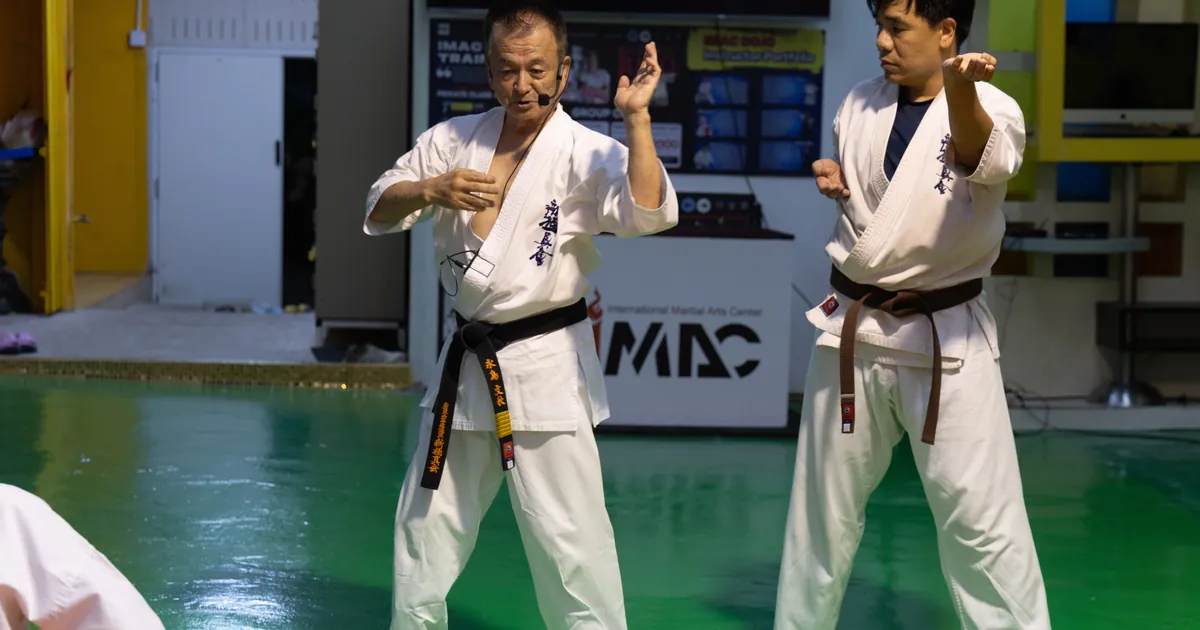 Shihan Fumiaki Frank Nagashima สาธิตท่า Kihon คู่กับครูสายน้ำตาลบนพื้นเขียวของ IMAC Dojo
